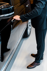 cropped image of businessman in suit opening door of black automobile