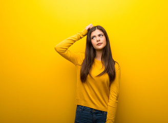 Teenager girl on vibrant yellow background having doubts while scratching head