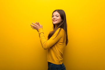 Teenager girl on vibrant yellow background applauding after presentation in a conference