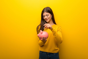 Teenager girl on vibrant yellow background taking a piggy bank and happy because it is full