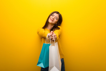Fototapeta na wymiar Teenager girl on vibrant yellow background holding a lot of shopping bags