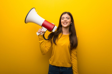 Teenager girl on vibrant yellow background holding a megaphone
