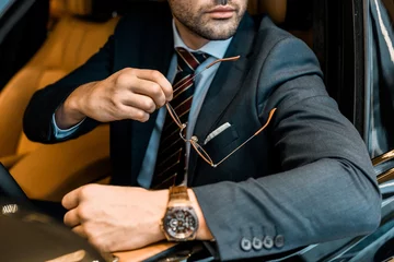 Foto op Plexiglas partial view of businessman with luxury watch holding eyeglasses while sitting in car © LIGHTFIELD STUDIOS