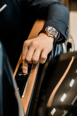 cropped image of businessman with luxury watch pushing button for closing window of automobile