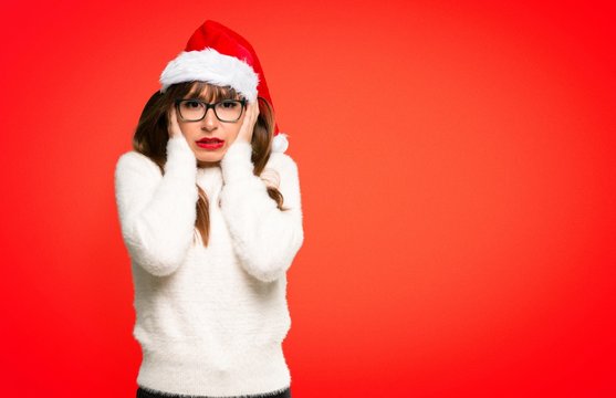 Girl with celebrating the christmas holidays covering ears with hands. Frustrated expression on red background