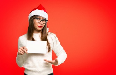 Girl with celebrating the christmas holidays holding an empty white placard for insert a concept on red background