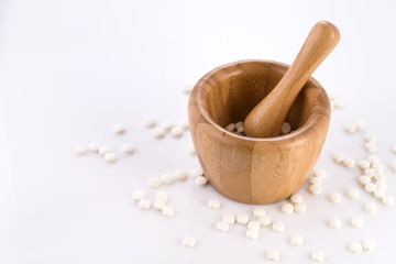 Close-up of small white tablets in a wooden mortar to be ground into powder. Preparation of medicinal mixtures.