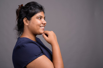 Young overweight beautiful Indian woman against gray background