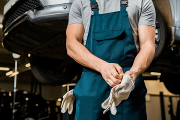partial view of auto mechanic in uniform wearing protective gloves at auto repair shop