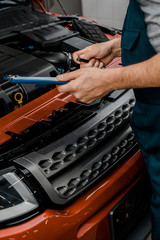 partial view of repairman with notepad examining car at auto repair shop