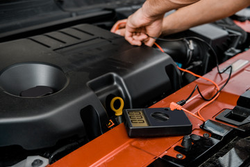 partial view of auto mechanic with multimeter voltmeter checking car battery voltage at mechanic shop
