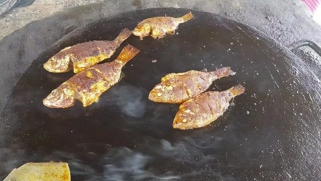 Spicy fish being fried in a big cast iron pan