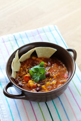Delicious chili con carne with tortilla in a clay bowl on wooden table