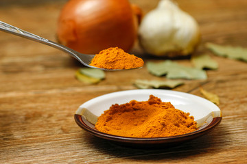 Metal spoon with turmeric spice on wooden table. Macro photography in rustic ambient.