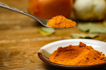 Metal spoon with turmeric spice on wooden table. Macro photography in rustic ambient.