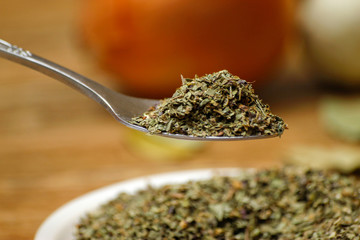 Dry basil spice in metal spoon and ceramic plate on wooden table and garlic and onion in the...