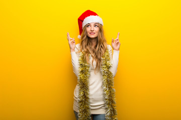 Girl celebrating the christmas holidays on yellow background with fingers crossing and wishing the best