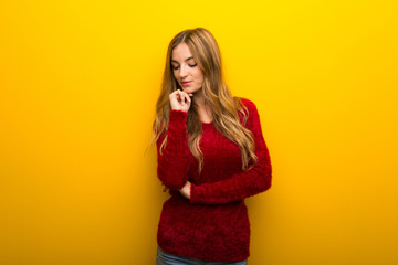 Young girl on vibrant yellow background looking down with the hand on the chin