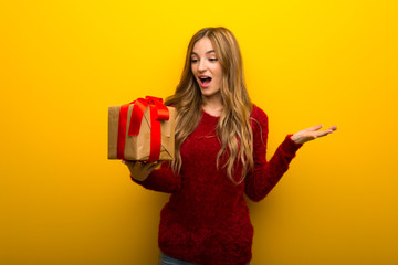 Young girl on vibrant yellow background holding gift box in hands