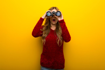 Young girl on vibrant yellow background and looking in the distance with binoculars