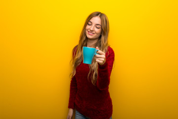 Young girl on vibrant yellow background holding a hot cup of coffee