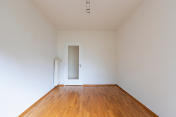 Empty room with white walls, parquet floor and wooden door