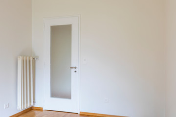 Empty room with white walls, parquet floor and wooden door