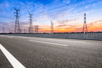Fototapeta na wymiar Asphalt road and high voltage power towers at sunset