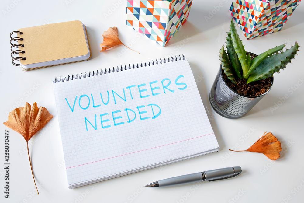 Poster volunteers needed written in a notebook on white table