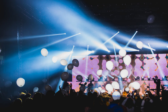 White balloons on the air at big indoor party. Crowd silhouette and hands