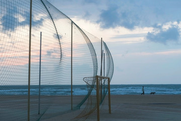 Sports ground with net and gate on the seashore. A man walks with a dog along the coast.
