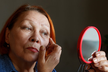 Elderly woman examines her wrinkles in the mirror