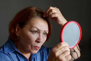 Naklejka premium Elderly woman looking at gray hair in her hair looking in the mirror