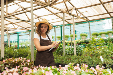 Naklejka na ściany i meble Happy young woman working in a greenhouse