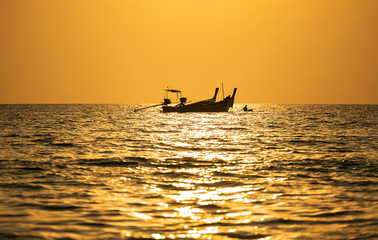 Silhouette fishing Long-tail boats in the Andaman Sea are floating to catch fish with the golden background of the sun on a nice day in Fisheries and Lifestyle concept .