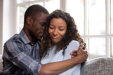 Loving African American husband embracing wife after quarrel, feeling guilty, asking forgive, saying sorry, doubting attractive woman thinking about compromise, relationships problem concept - obrazy, fototapety, plakaty
