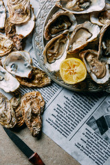 flat lay with oysters, lemon and knife on newspaper on grey surface