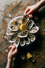 partial view of women at grungy tabletop with oysters, ice and lemon