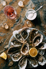 flat lay with glass of wine, oysters with ice and lemon pieces on grungy tabletop