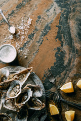 top view of arrangement of oysters and lemon pieces on grungy tabletop