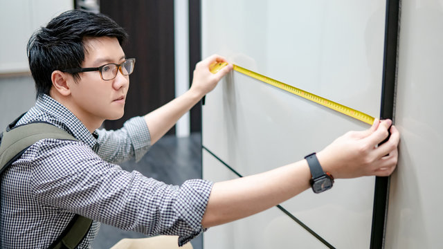 Young Asian Man Using Tape Measure For Measuring Modern Cabinet In Walk-in Closet Showroom. Shopping Furniture For Home Improvement. Interior Design Concept