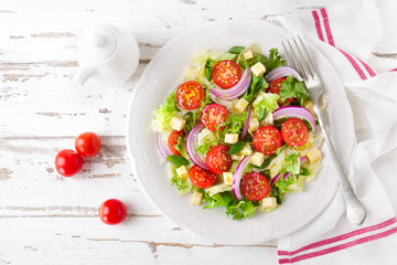 Fresh vegetable salad with tomatoes, lettuce, onion and cheese on white wooden background. Healthy vegetarian food. Top view