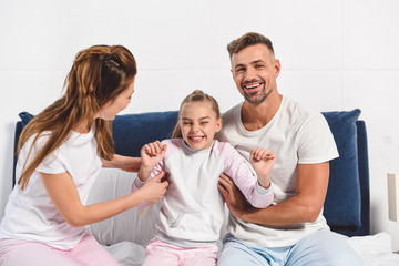 smiling parents tickling preteen daughter in bed - obrazy, fototapety, plakaty