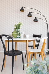 Black and white chair at wooden table in dining room interior with plants and lamp. Real photo