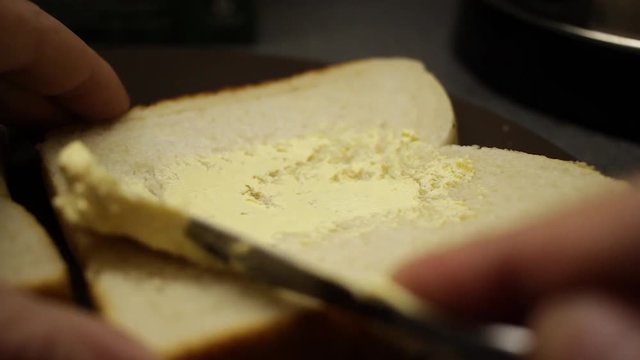 Close up of a man's hand spreading butter onto a piece of white bread.