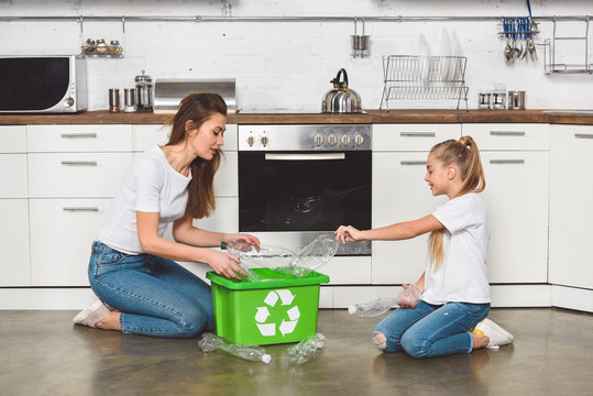 mother and daughter putting empty plastic bottles at green recycle box at kitchen