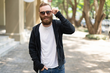 Joyful bearded hipster singing outdoors. Positive young man wearing sunglasses talking to camera....