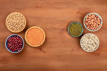 Various types of pulses, shot from above on a dark rustic wooden background with copy space. Red kidney, pinto, and black beans, lentils, chickpeas, soybeans, black-eyed peas, forming a frame