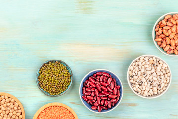 Various types of pulses, shot from the top on a teal background with a place for text. Red kidney and pinto beans, lentils, chickpeas, soybeans, and black-eyed peas