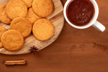 A closeup of gingersnaps with a mug of hot chocolate, a cinnamon stick, and an anise star, shot from above on a dark rustic background with copy space